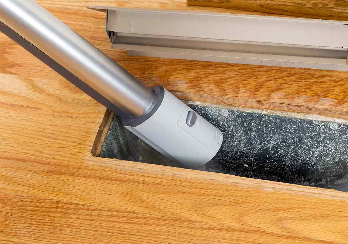Vacuum hose cleaning dust from a floor air vent
